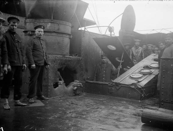 Shell hole in a casemate on HMS Kent made during the Battle of the Falkland Islands on 8th December 1914. Sergeant Mayes RMA stands to the left of the hole